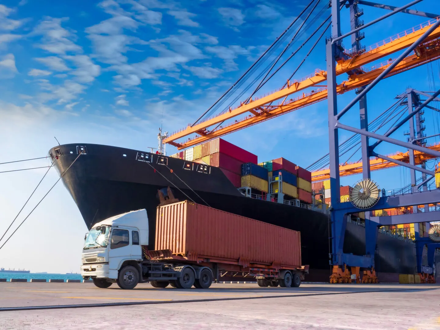 Container ship at berth beneath quay cranes, with a container truck on the quay