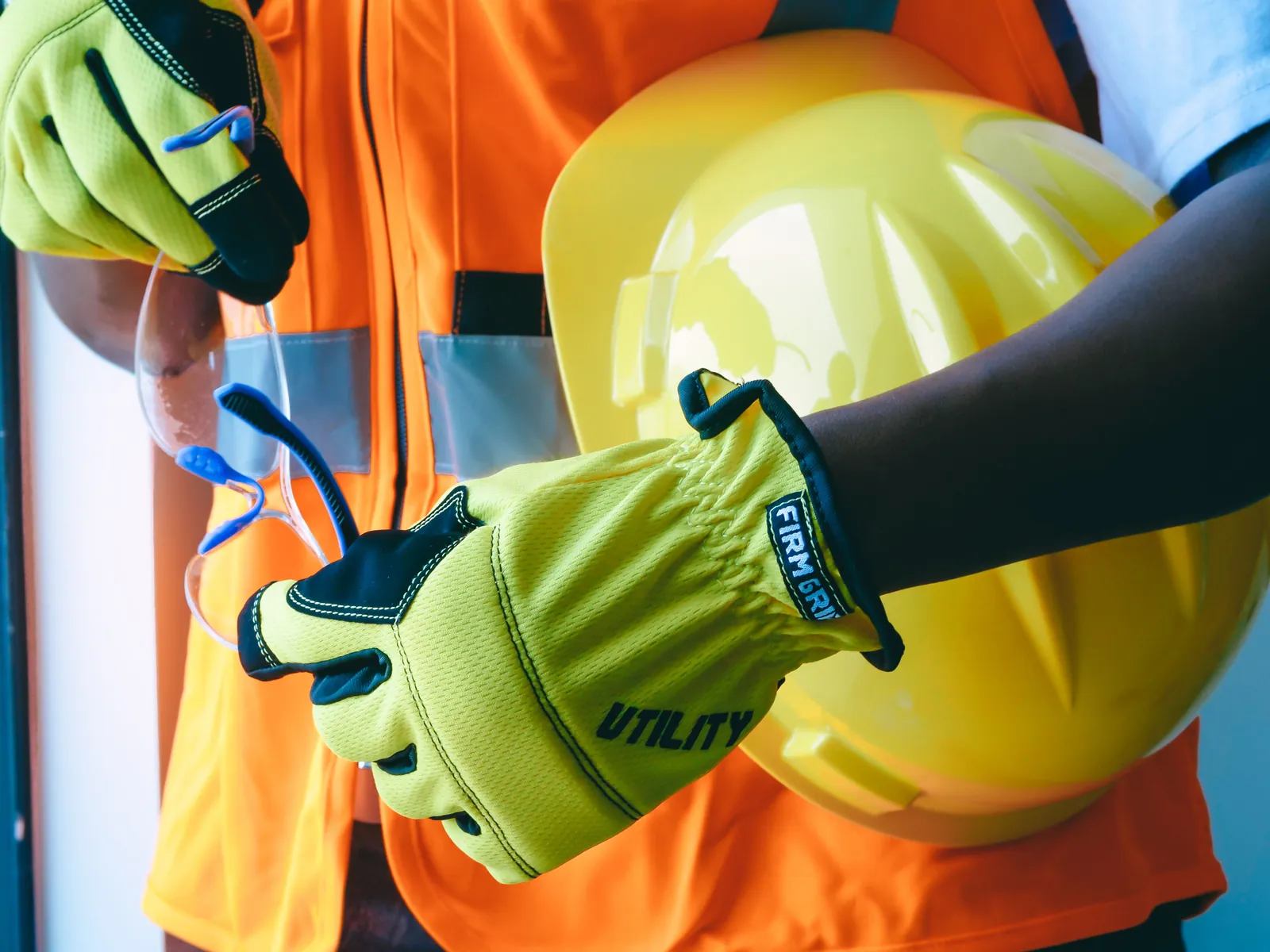 Worker in a high-visibility vest holding a safety helmet and protective gloves